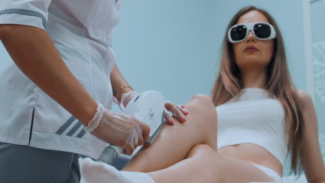 Laser-hair-removal-on-ladies-legs.-The-girl-is-lying-on-the-couch-in-the-medical-glasses-in-the-treatment-room.-The-hands-of-the-cosmetologist-make-the-epilation-of-the-legs